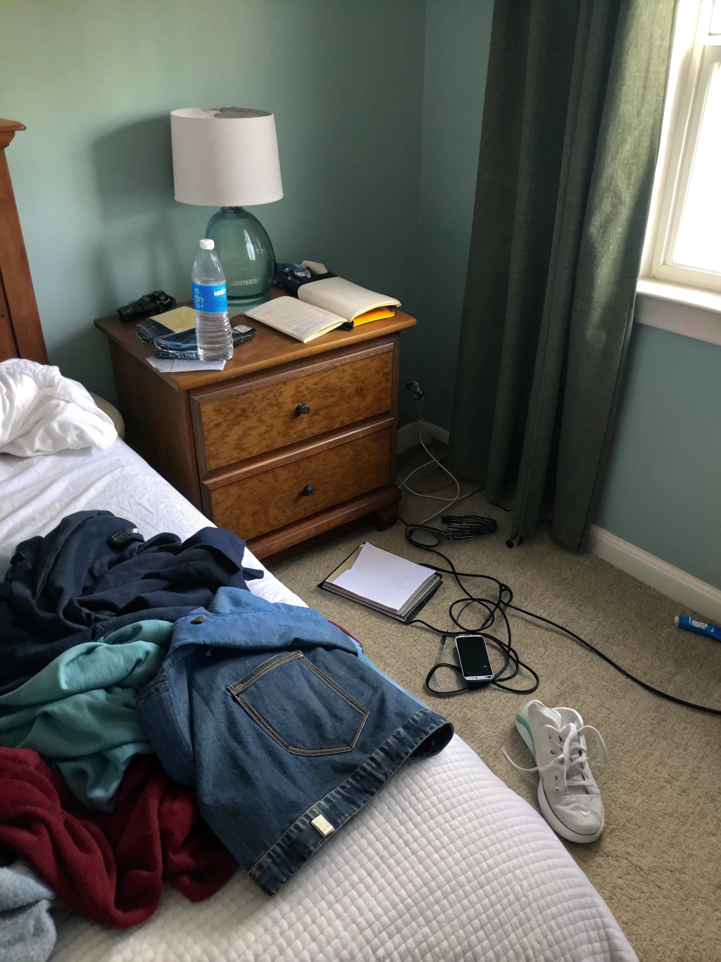 Unmade bed with thin cyan predawn light through curtain gap and rumpled sheets